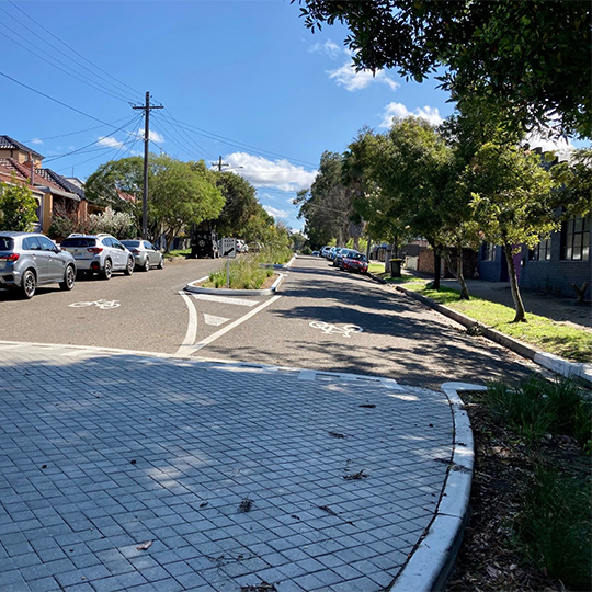 A local street with a landscaped central median and a raised paved street treatment.
